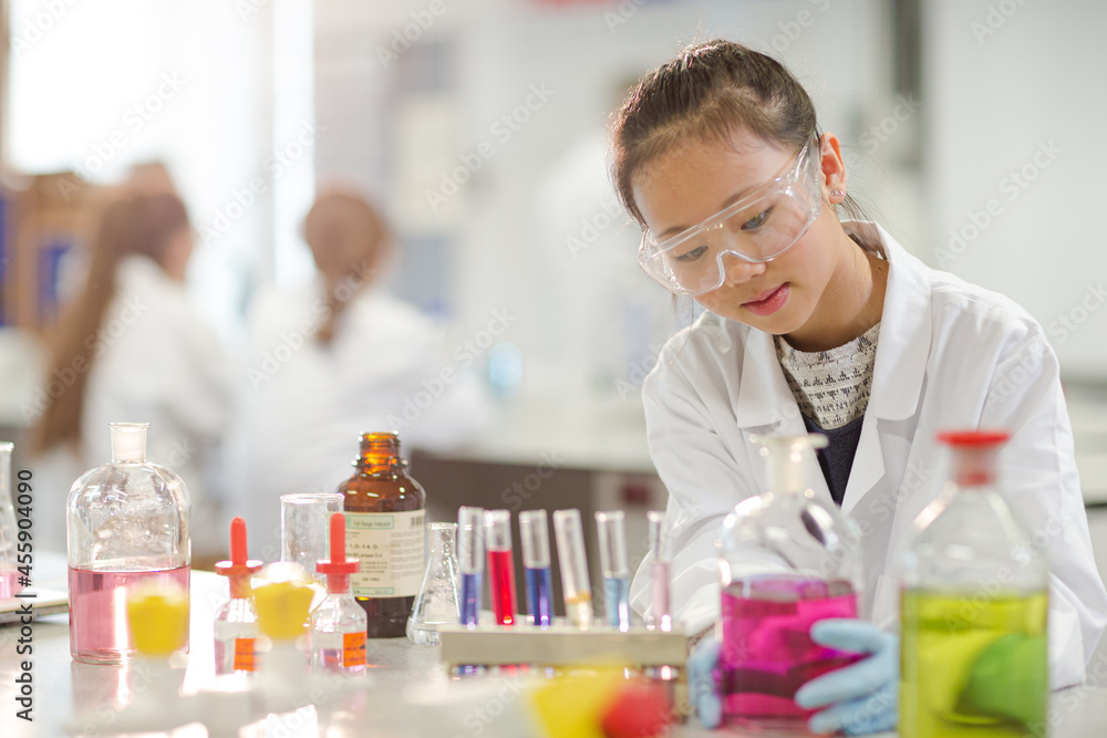 Girl student examining pink liquid, conducting scientific experiment in ...
