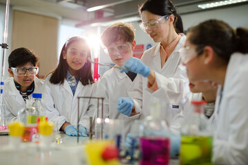 Wall Mural - female teacher and students conducting scientific experiment, watching liquid in test tube in labora