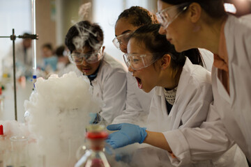 female teacher and students watching scientific experiment chemical reaction in laboratory classroom