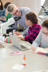 Wall Mural - male teacher and girl students conducting scientific experiment at microscope and laptop in laborato