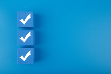 modern minimal flat lay with three white checkmarks on blue cubes against blue background with copy 