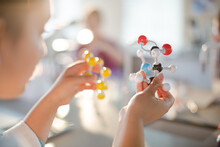 Curious Girl Student Holding Molecule Model In Classroom
