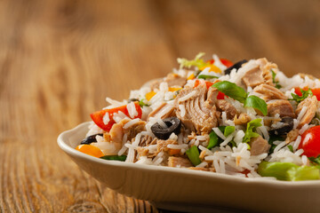 Italian tuna salad with rice, olives and capers. Front view. Natural wooden background.