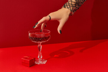 Womans hand with spooky nail design take glass with cranberry halloween cocktail on red background