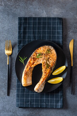 Wall Mural - Fresh cooked delicious salmon steak with spices and herbs. Healthy seafood. Restaurant menu, recipe. Roasted trout steak served on a black plate. Top view, vertical, close up