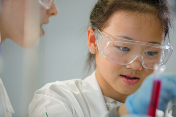 girl student examining pink liquid, conducting scientific experiment in laboratory classroom