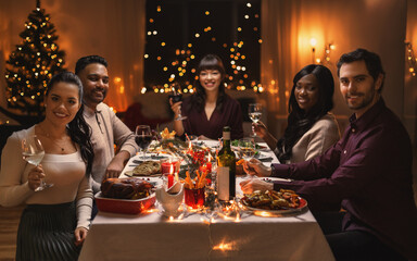 Wall Mural - holidays, party and celebration concept - multiethnic group of happy friends having christmas dinner at home and drinking wine