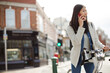 © KOTO - Smiling young woman commuting on bicycle, talking on cell phone on sunny urban street