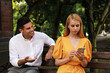 Young woman with smartphone ignoring her boyfriend in park. Boring date