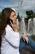 © fotodiya83 - Young beautiful woman talking on a smartphone while sitting near a fountain on the street.