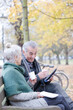 © KOTO - Senior couple reading newspaper and drinking coffee on bench in autumn park