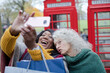 Senior women friends with shopping bags taking selfie in autumn park in front of red telephone booths