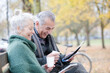 © KOTO - Senior couple reading newspaper and drinking coffee on bench in autumn park