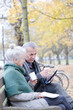 © KOTO - Senior couple reading newspaper and drinking coffee on bench in autumn park