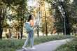 © LIGHTFIELD STUDIOS - smiling asian woman in jeans walking in park with backpack and notebooks