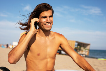 Portrait of handsome surfer with his surfboard. Young man talking to the phone