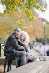 Wall Mural - Active senior couple talking, enjoying coffee at autumn park cafe