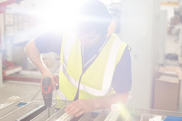 Wall Mural - Male engineer with power drill assembling equipment in steel factory