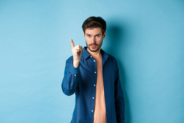 Serious young man scolding person, shaking finger disapprovingly, warn or prohibit something bad, standing on blue background