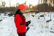 Female Runner Checking Mobile While Running in Woods. Sportswoman With Trekking Poles Holding Cellphone in Hands On Cold Winter Day.