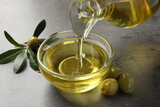Fototapeta  - Pouring olive oil into glass bowl on grey table, closeup