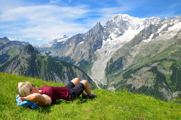 Wall Mural - Tourist lying on a meadow in sunny day, at the background Mont Blanc ( Monte Bianco ) mountain range. Aosta valley, Italy.