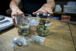© ADDICTIVE STOCK - Crop man with jars of dry marijuana flowers in workspace