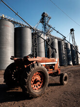 Old Red Work Tractor Parked In Front Of Several Steel Grain Silos On Farm