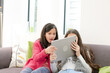 © KOTO - Happy sisters using digital tablet on living room sofa