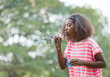 © amorn - Little African American girl blowing soap bubbles in the park.