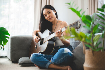 Asian woman playing music by guitar at home, young female guitarist musician lifestyle with acoustic art instrument sitting to play and sing a song making sound in hobby in the house room