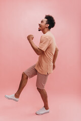 Wall Mural - full length happy black guy in pink fashionable clothes on isolated background. cheerful smiling young African American male model is actively moving in studio.