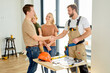 © Roman - Builder Repairman In Overall Working Uniform Shake Hand To Clients Family After Agreement, After Sharing Ideas Of House Planning, Home Improvement. Side View