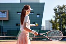 View From Back On Pretty Young Woman In Sexy Sportwear Playing Tennis In City Park At Summer Day. Redhead Female Tennis Player With Racket, Enjoying Game, Looking At Side. Sport, Healthy Lifestyle