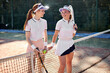 © Roman - Beautiful fit female tennis players playing doubles at tennis at the tennis court, attractive ladies in white uniform stand together before competition, posing, holding racket in hands. portrait