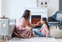 Young Mother And Daughter Resting Near Fireplace At Home