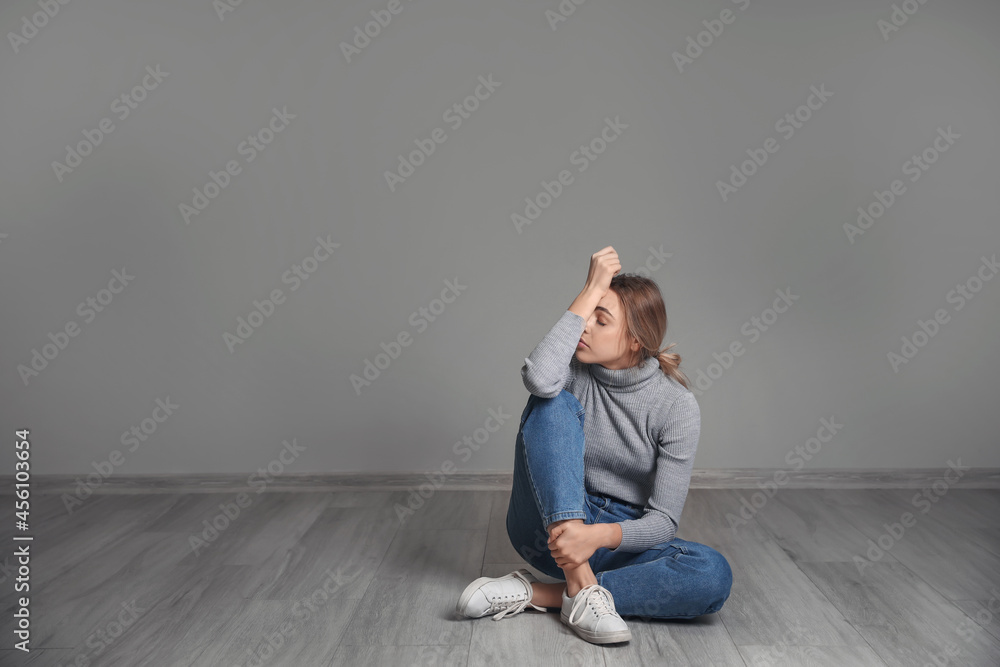 Depressed young woman sitting on floor near grey wall