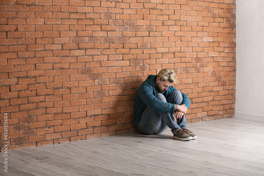 Depressed young man sitting near brick wall