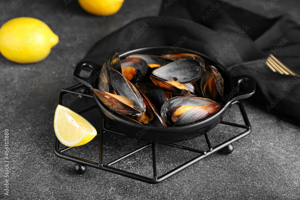 Frying pan with tasty mussels and lemon on dark background