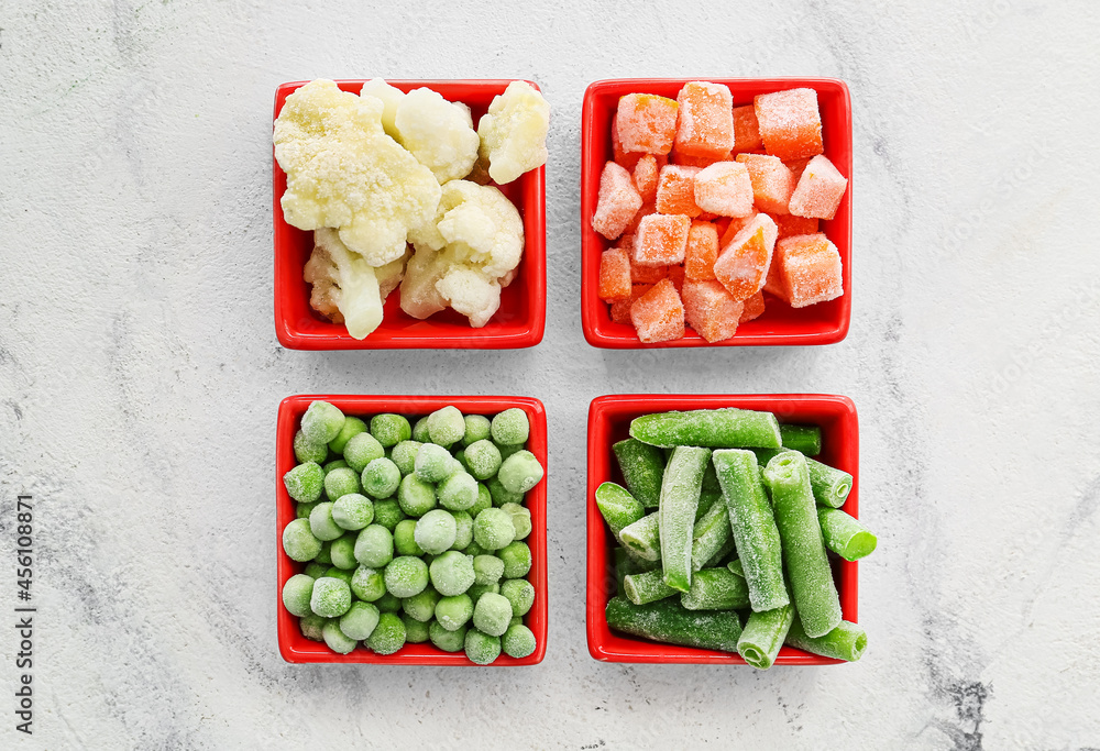 Bowls with different frozen vegetables on light background