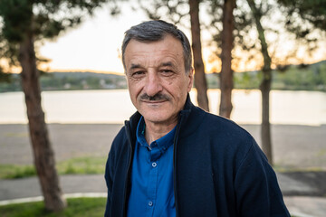 Portrait of senior caucasian man in nature standing in spring or autumn day - close up of cheerful male standing looking to the camera - real people concept