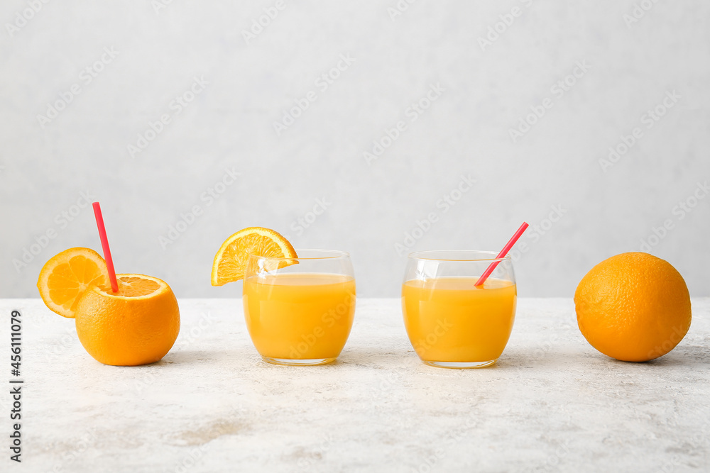 Glasses of tasty orange juice on light background