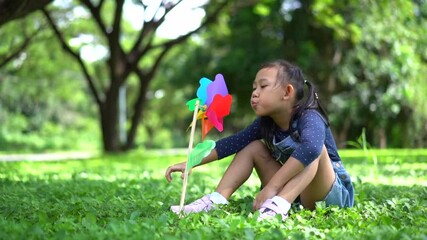 Wall Mural - Slow motion Happy Asian little girl playing with paper windmill in the garden