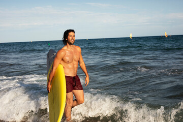 Portrait of handsome surfer with his surfboard. Young man with a surfboard on the beach.