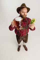 Wall Mural - Young bearded man, waiter in traditional Bavarian costume holding beer glasses filled with wild hot and lager. Celebration, oktoberfest, festival concept.