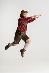 Wall Mural - Full-length portrait of bearded man in hat and traditional Bavarian costume jumping high isolated over white background. Flyer, oktoberfest concept