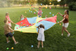 © New Africa - Group of children and teachers playing with rainbow playground parachute on green grass. Summer camp activity
