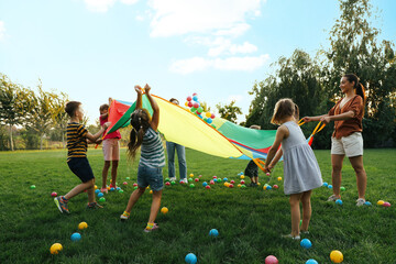 Wall Mural - Group of children and teacher playing with rainbow playground parachute on green grass. Summer camp activity