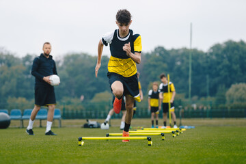 Wall Mural - Junior soccer player running fast and ladder skipping. Boys practice football witch young coach. Teenagers on soccer training camp. Youth athletes improving soccer skills on outdoor training