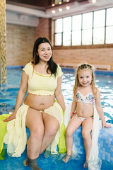 young pregnant mother with a girl by the indoor pool. mother and daughter are preparing to swim.